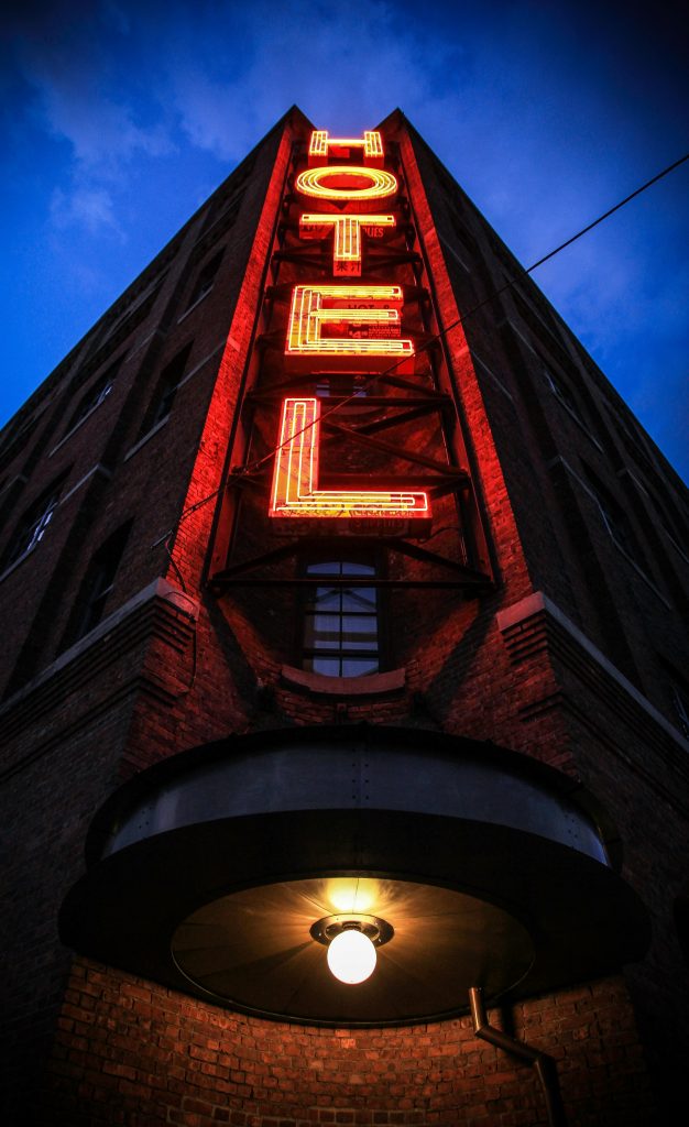 Eye-catching low angle shot of a neon hotel sign illuminating a brick building facade at dusk.